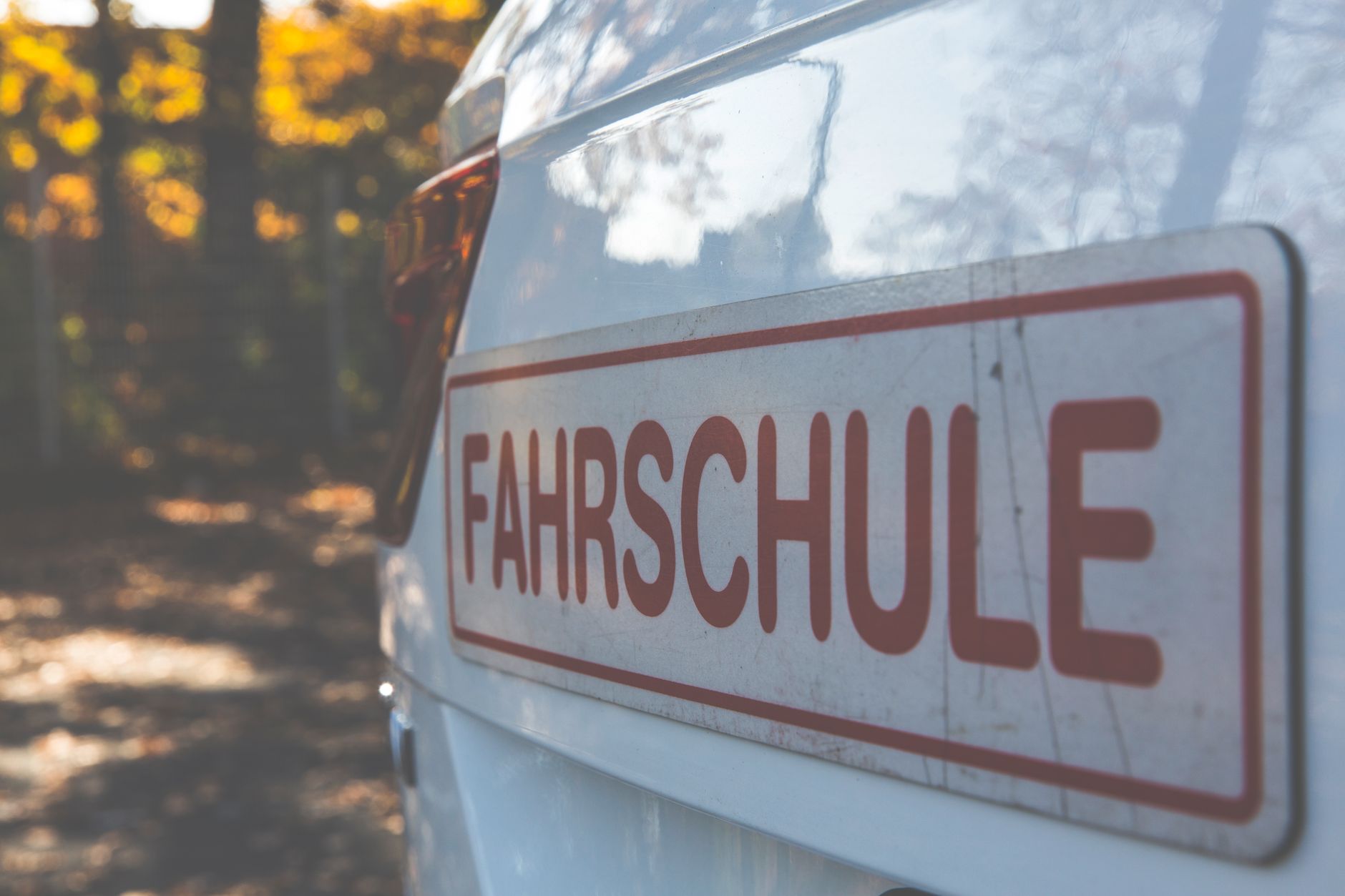 A driving-school car with a roof sign parked on a tree-lined road, dual controls and an instructor the only difference that matters