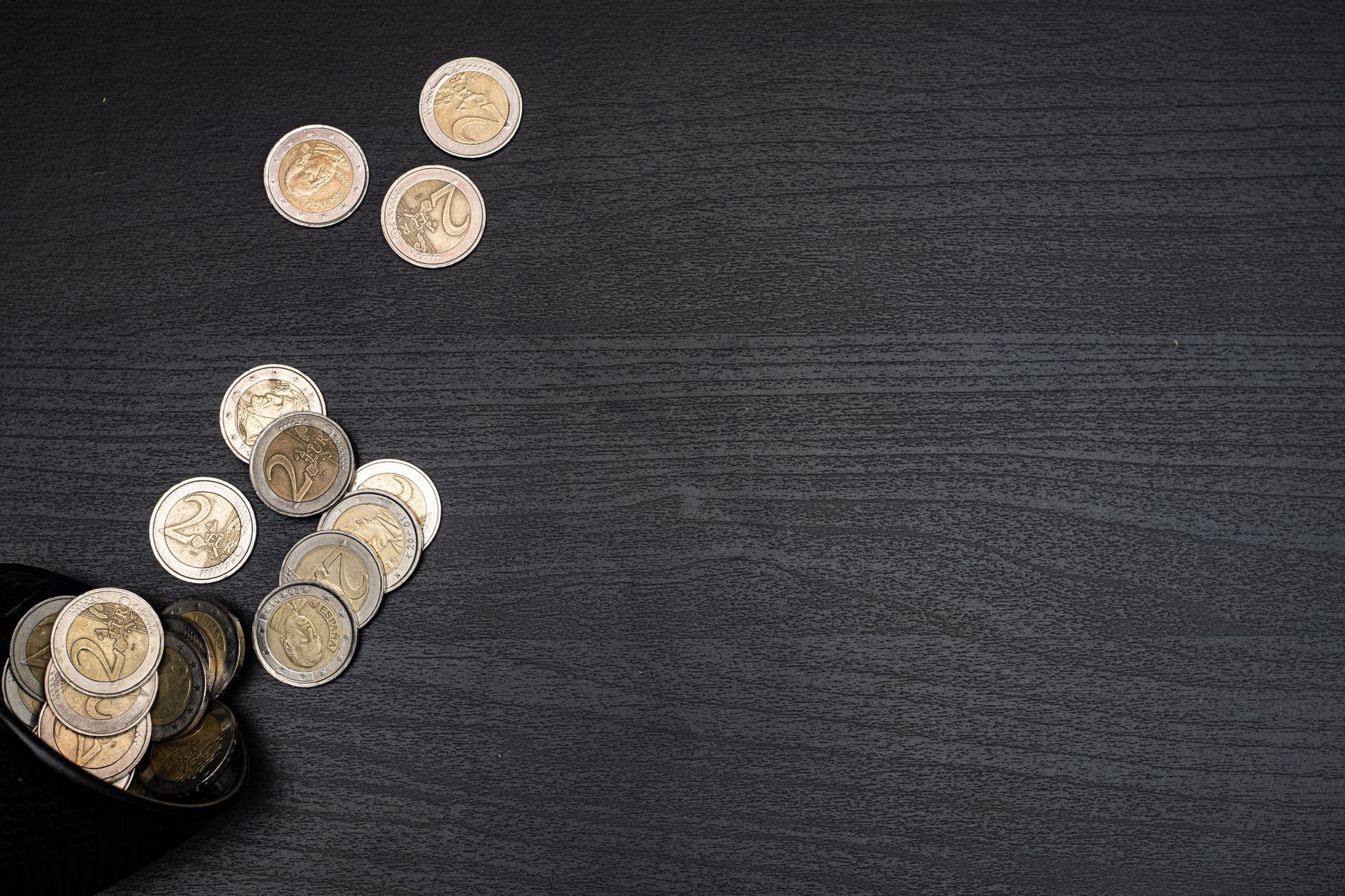 Euro coins scattered across a dark surface, the sum a new driver hands over before they've driven a mile