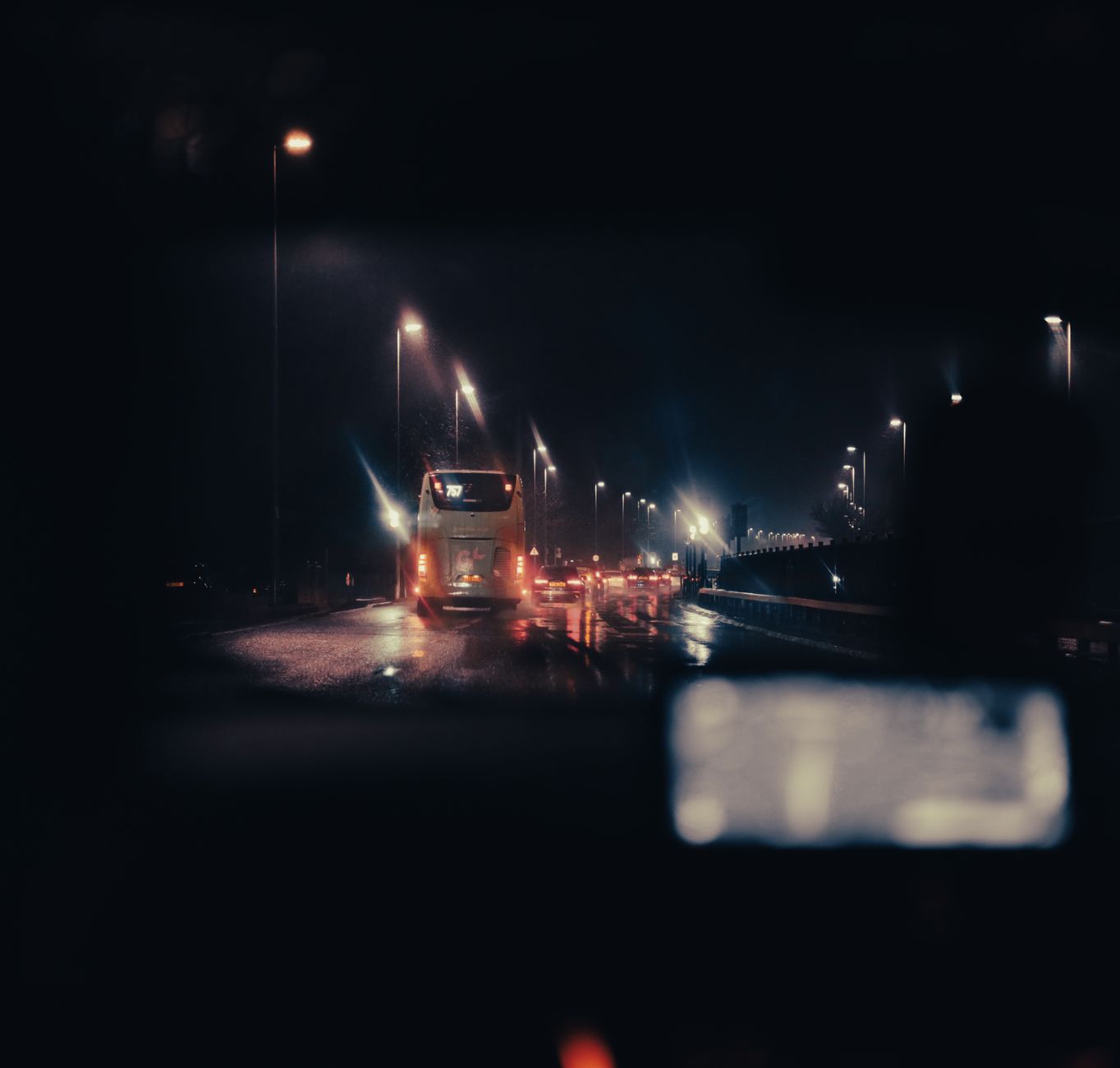 View through a windscreen of a dark road at night lit by headlights and streetlights