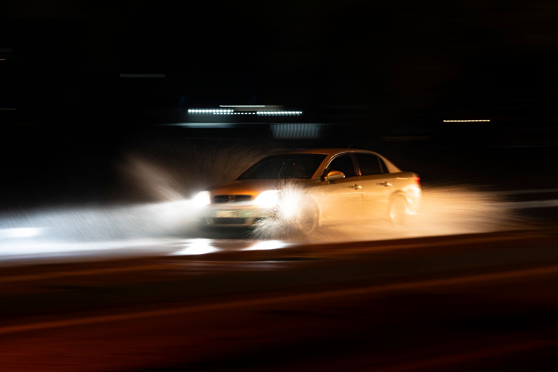A car on a wet road at night, headlights throwing spray, the kind of surface that punishes a driver who is not reading ahead