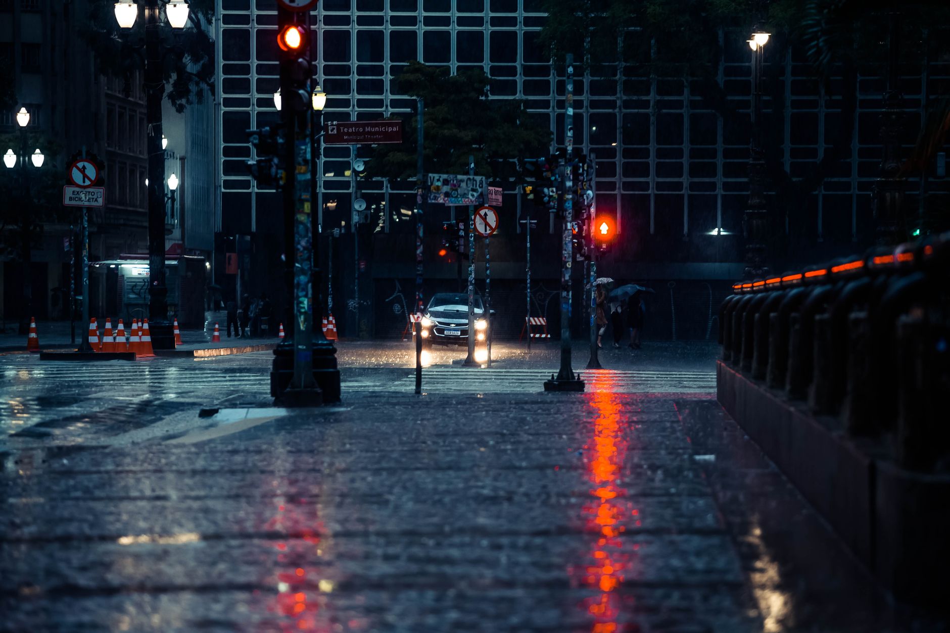 A wet urban street at night with traffic signals reflected on the road, the rules-heavy world a new permit-holder enters