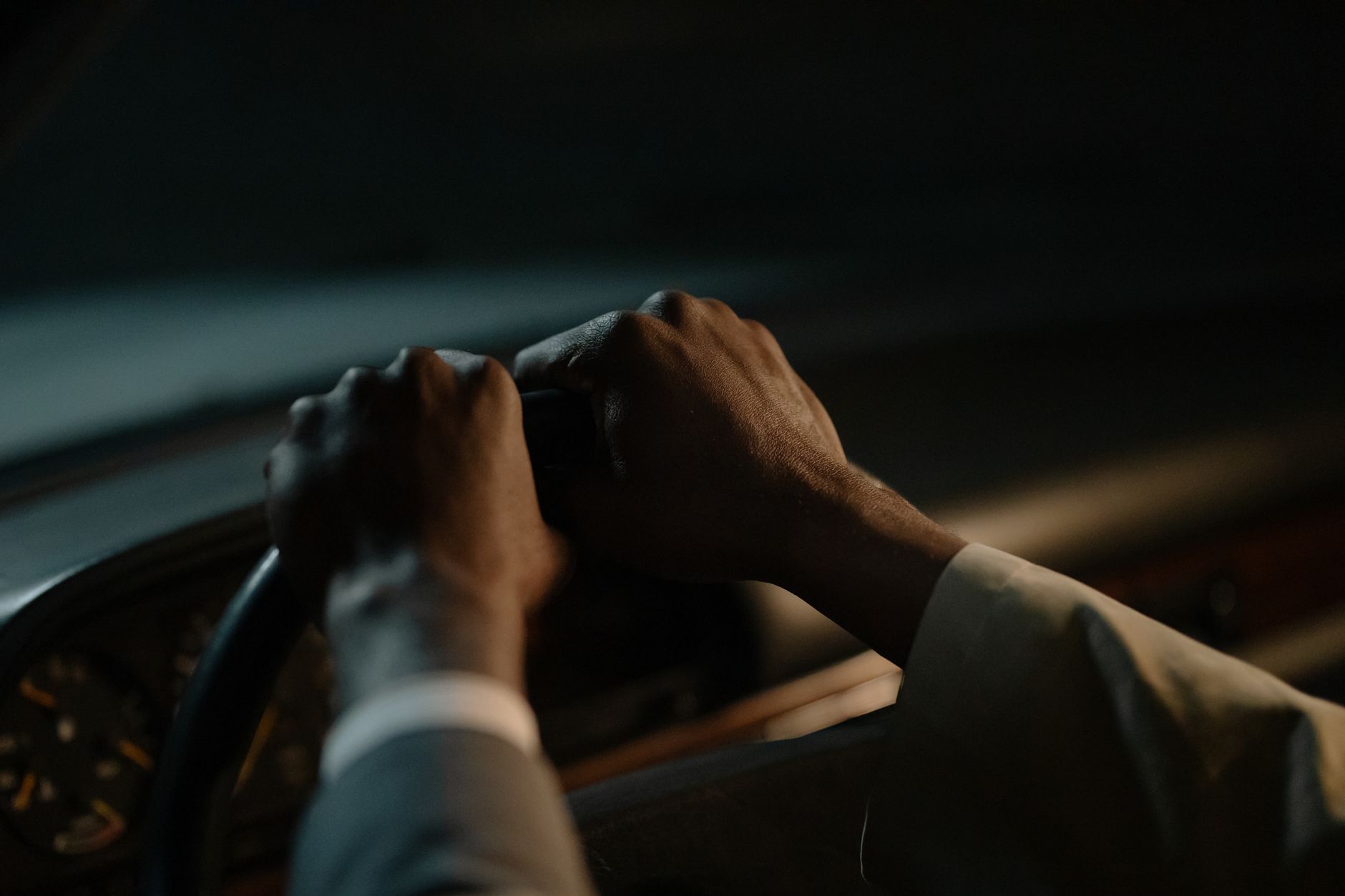 A driver's hands at ten-to-two on the wheel in a dim car interior, focused and deliberate
